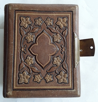An old small tan elaborately decorated thick photograph album with family photos.