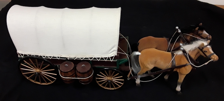 A model of a long fabric covered Conestoga Wagon with two horses, brown and tan. 