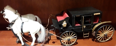 A model of a black enclosed coach and two white horses which is a four wheeled passenger horse drawn vehicle.