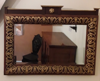 A beautifully carved wooden framed mirror featuring a gold painted carved lion head and painted crest style decoration.