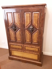 A heavily inlaid veneer two door cabinet with carved Egyptian style heads in the middle of each door set in a triangular pattern. 