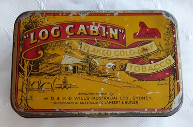 A small rectangular, metal 'Log Cabin' tobacco tin with red edging around the yellow, hinged lid.
