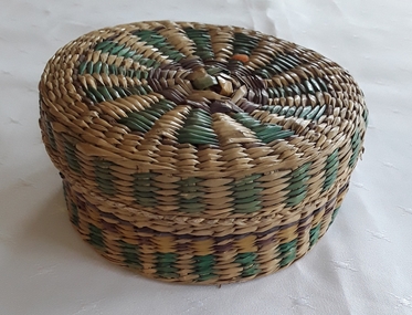 A small natural, green and purple coloured raffia lidded basket with embroidery threads inside.