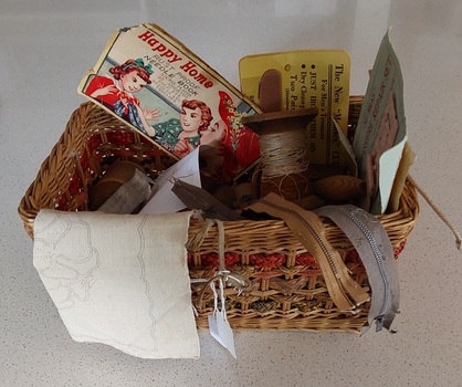 An open rectangular shaped cane woven sewing basket with three bands of green and tan raffia woven around the sides. 