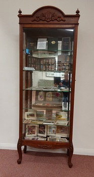 A tall wooden vintage display cabinet with an ornately carved top with four filials on each corner and decorative shaped legs. 