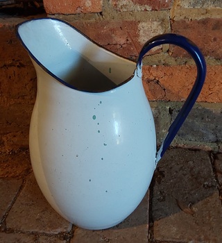 A large white enamel water jug or pitcher with a dark blue handle and dark blue trim.