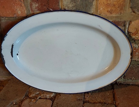 A large oval white enamel serving tray with navy blue edging on the rim.