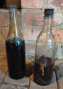  Two vintage glass cordial bottles with embossed patterns; one a leaf design, the other of squares.