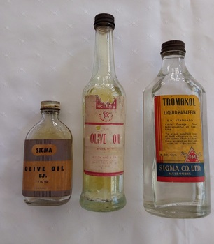 Three clear glass bottles, two containing medicinal olive oil and one with liquid paraffin. 