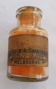 A small squat clear glass bottle with a cork stopper and orange coloured food powder inside.. 