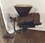 A small cast iron mincer with a wooden handle attached to the long cast iron handle.