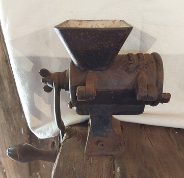 A small vintage cast iron mincer with a wooden handle attached to the long cast iron handle.