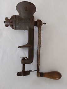 A vintage cast iron mincer with a wooden handle attached to the long cast iron handle.