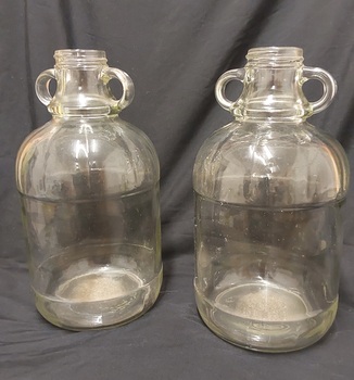 Two large heavy glass wine flagons, with two handles at the top of each.