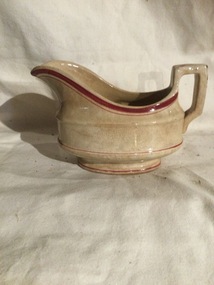 An aged faded white ceramic gravy boat (no saucer) with two red stripes on the rim and two red lines around the body. 