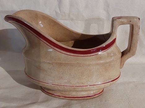 An aged faded white ceramic gravy boat with two red stripes on the rim and two red lines around the body. 