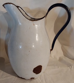 A large white enamel water jug or pitcher with a dark blue handle and dark blue trim. 