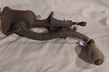 A vintage cast iron mincer with a wooden handle attached to the long cast iron handle. 