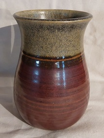 A small plain brown pottery vase which is darker brown at the bottom and lighter speckled at the top.