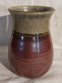 A small plain brown pottery vase which is darker brown at the bottom and lighter speckled at the top.