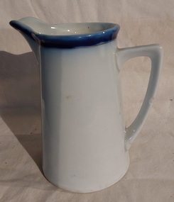 A medium sized ceramic white jug with a blue band around the top trimmed with a gold line on the rim. 