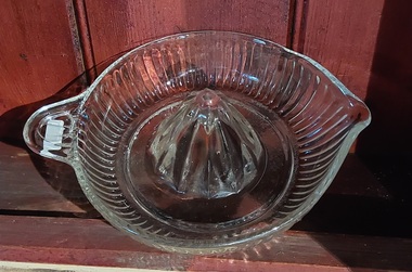 A large clear glass citrus juicer with decorative lined ridges around the sides of the bowl to collect the juice.