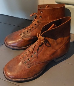 A pair of handmade brown leather work boots, with brown leather laces and decorative stitching. 