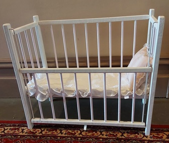 A lilac and white painted wooden dolls cot with an eight railed drop side, a wooden base with four white slats. 