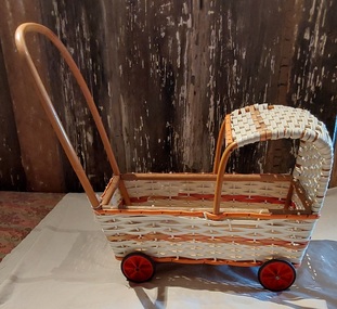 A plastic white wicker dolls pram with orange and tan trim on the hood and carriage.