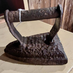 An antique heavy cast iron, sad iron, with a roughened surfave and a rounded cast iron handle.