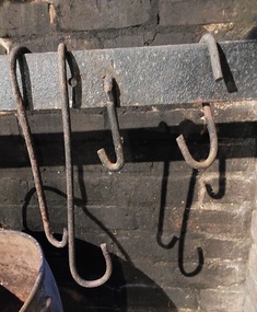 Two antique 'S' shaped removable cast iron hooks used to hang heavy cast iron cooking utensils over an open fire in the home kitchen.