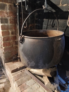 A large antique black oval cast iron Boiler Pot with small curved lifting handles on the sides and a long curved carrying handle on top. 