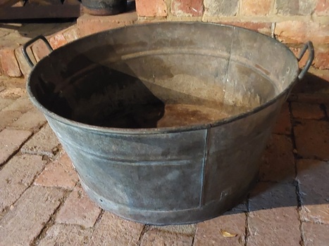 A large vintage round galvanised iron tub tapering slightly to the flat base.