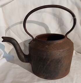 A large vintage rusted black cast iron heavy kettle with no lid. It has a flat base and mushroom shaped handle welded onto the pot below the rim of the pot opening. 