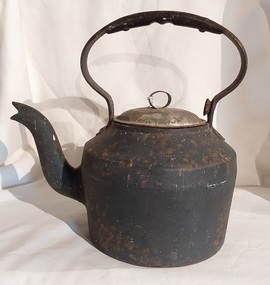 A large heavy black cast iron kettle with a curved handle and a removable lid with a small looped open knob.