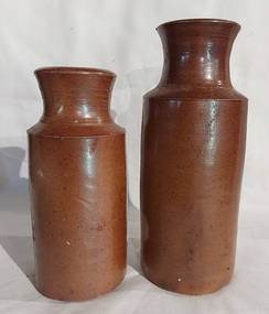 Two brown pottery blacking bottles, one with a light brown glaze and other is dark brown.