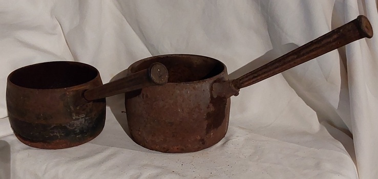 Two vintage black sooted heavy cast iron cooking pots or saucepans with rounded sides and long straight fluted handles.