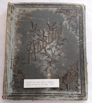 An antique dark green Album used as a scrapbook for many small coloured cut out stickers of flowers, children, animals and birds.