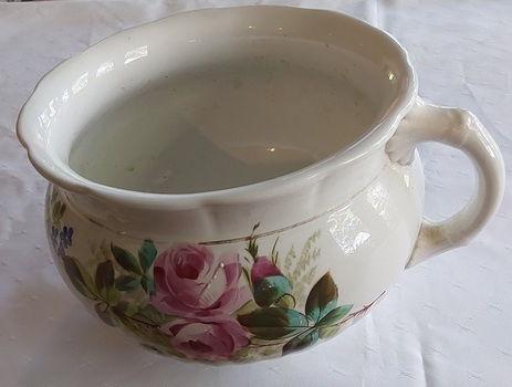 A white porcelain chamber pot decorated on two sides with large double pink roses and a blue floral leafed pattern.