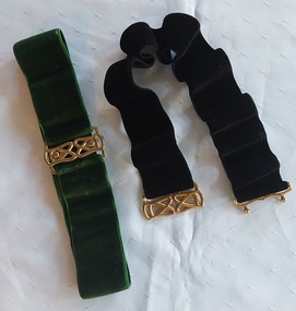 A homemade pair of wide elasticised velvet belts, one dark green and one black with ornate gold clip buckles.