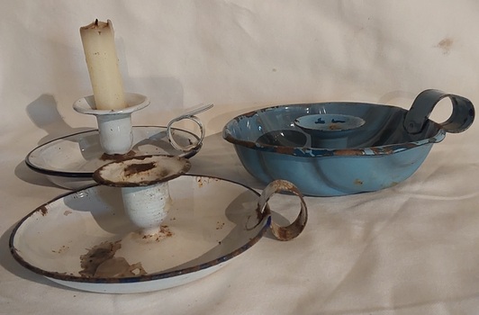 Three quite damaged enamelled metal candlestick holders with a plate-shaped base and a small finger handle at the side. 