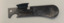A small metal Field Rations Eating Device (F.R.E.D.) with two sides, one side has a shallow spoon and the other a bottle opener.