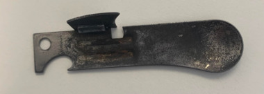 A small metal Field Rations Eating Device (F.R.E.D.) with two sides, one side has a shallow spoon and the other a bottle opener.