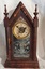 A small vintage decoratively carved dark timber steeple mantel pendulum clock with a white cardboard face, black roman numerals and black metal hands.