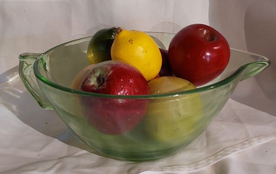 A vintage large round green Depression glass mixing bowl with a pouring lip and handle, used for cooking.