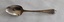A single silver teaspoon with engraving on the top of the handle and a maker's mark underneath.