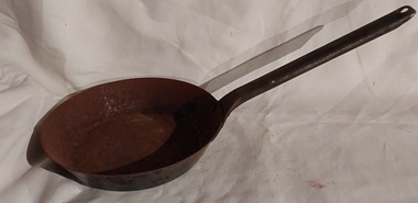 A shallow small cast iron frying pan with a long tubular handle attached with three rivets to the pan. 