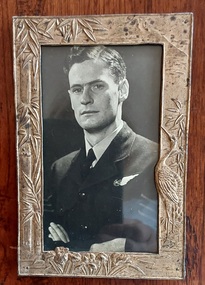 A decorative gold metal framed photo of Max Proctor in his RAF uniform with his arms folded.