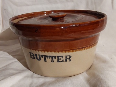A round two toned brown and cream lidded pottery butter dish.