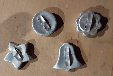 Four aluminium vintage biscuit or pastry cutters, including a star, bell, circle and flower shape with curved handles.